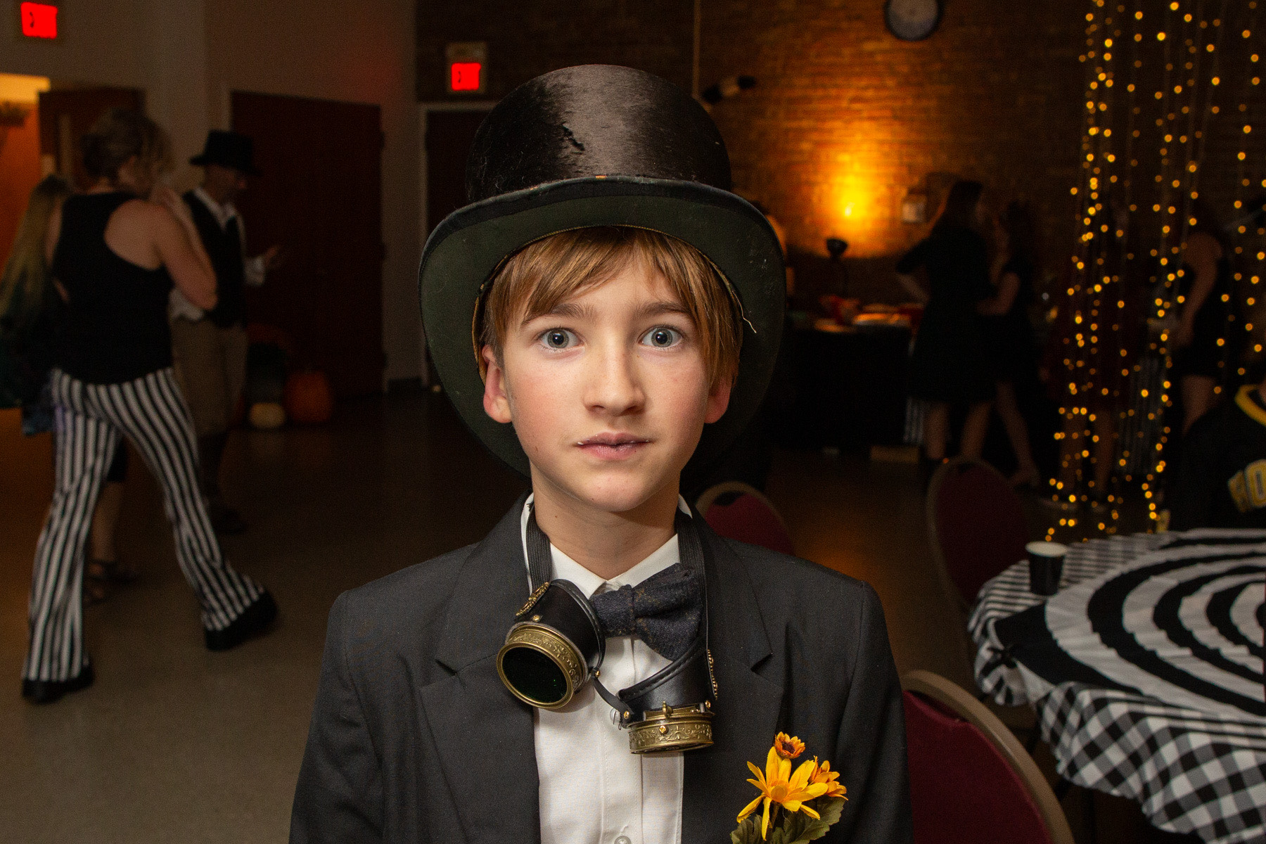 Kid dressed up in a top hat, bow tie, and steampunk goggles at the annual co-op school dance