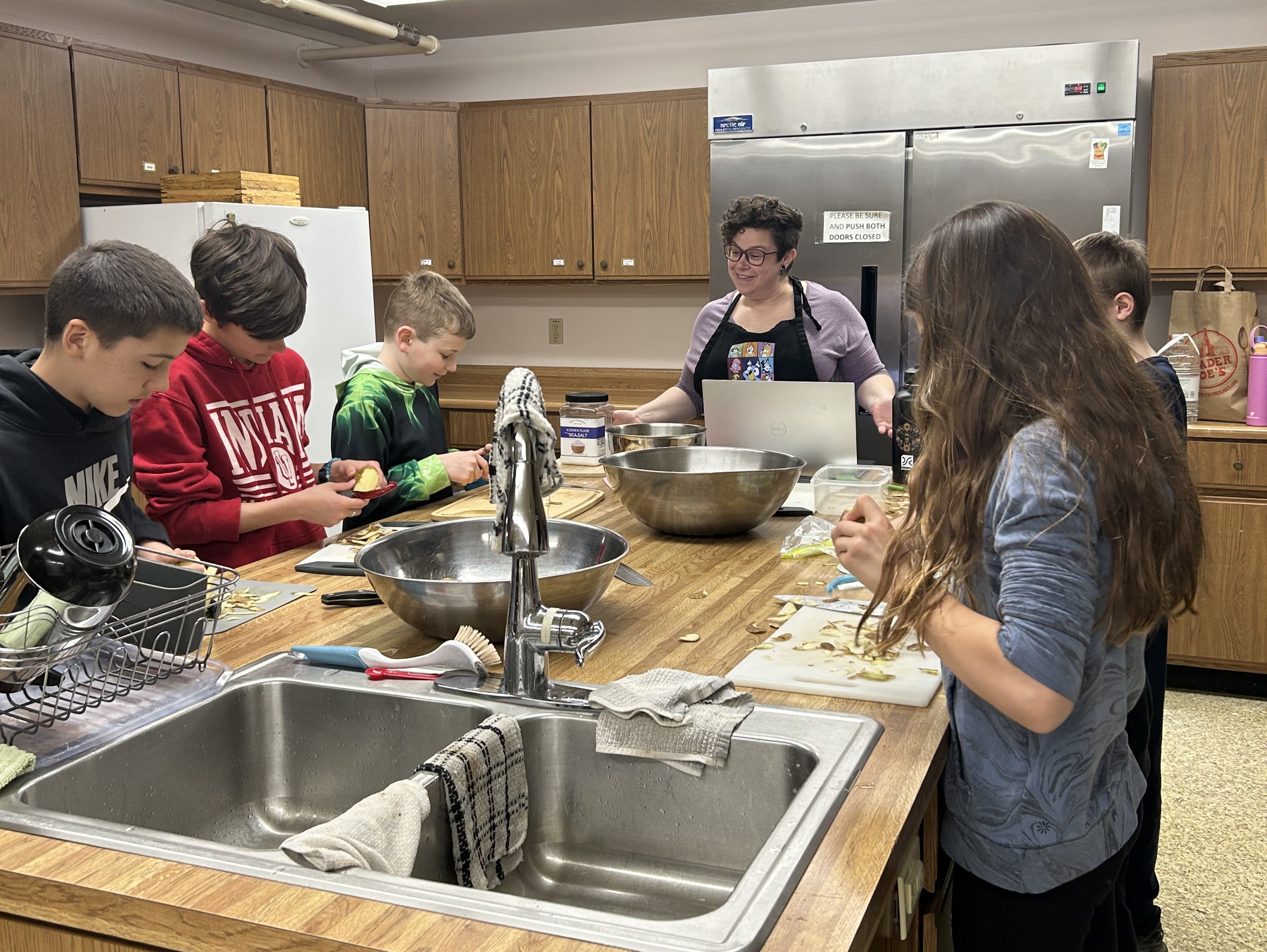Tweens and teens cooking together in the kitchen with a parent volunteer