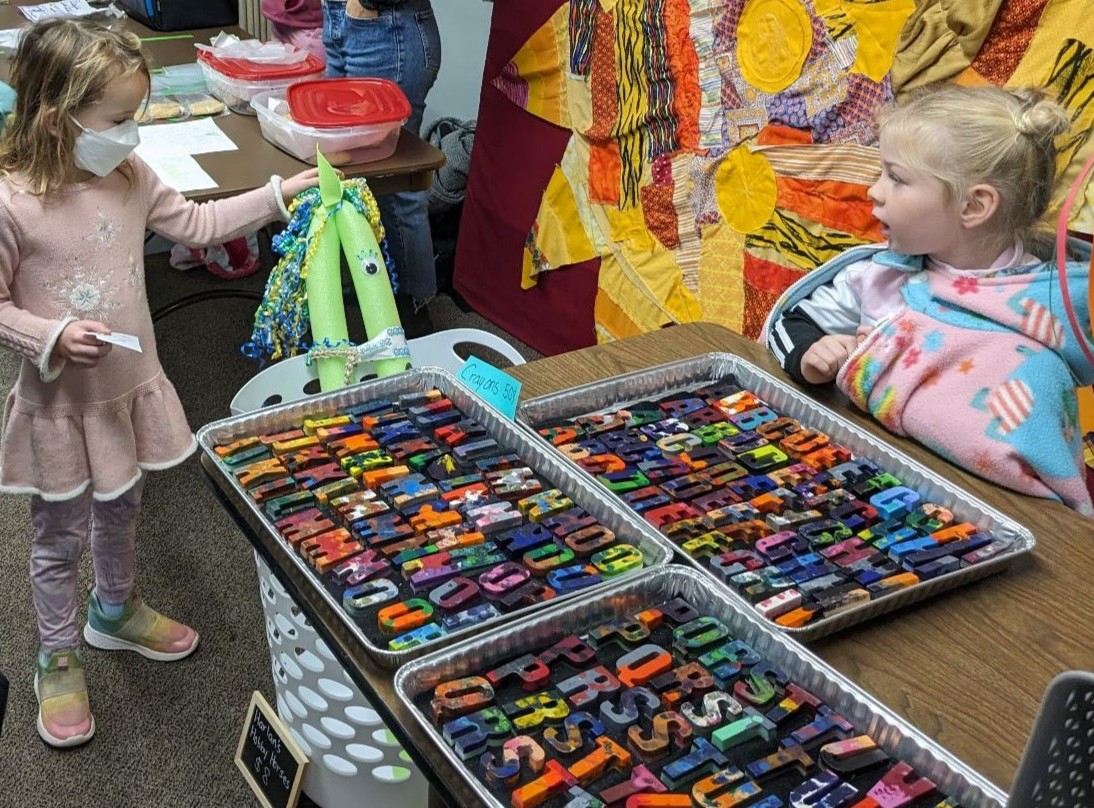 Young kids browsing colorful handmade crayon letters at the Maker's Market